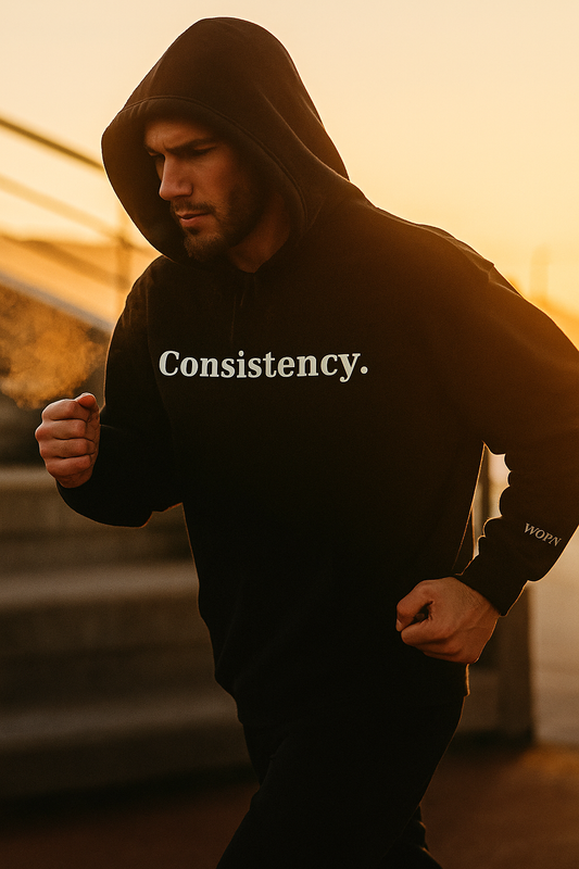Model running at sunrise wearing black motivational hoodie with consistency text, Worn Theory Fit State collection.